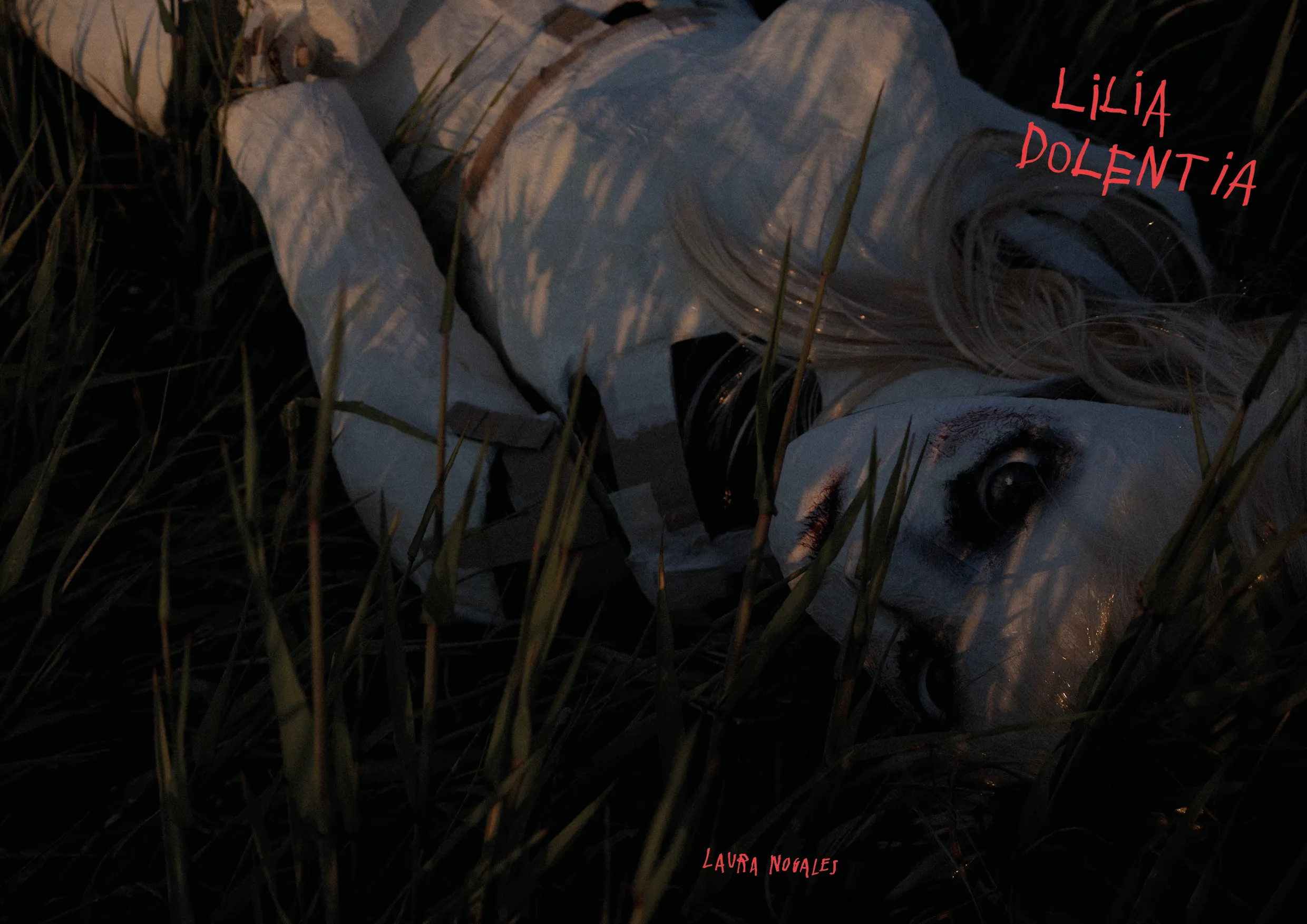 Portada del fotolibro "lilia dolentia" imagen de una muñeca de papel a escala real tumbada en una pradera